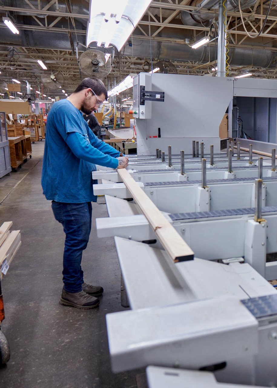 A photo of a young man marking up a piece of wood next to a high tech machine.